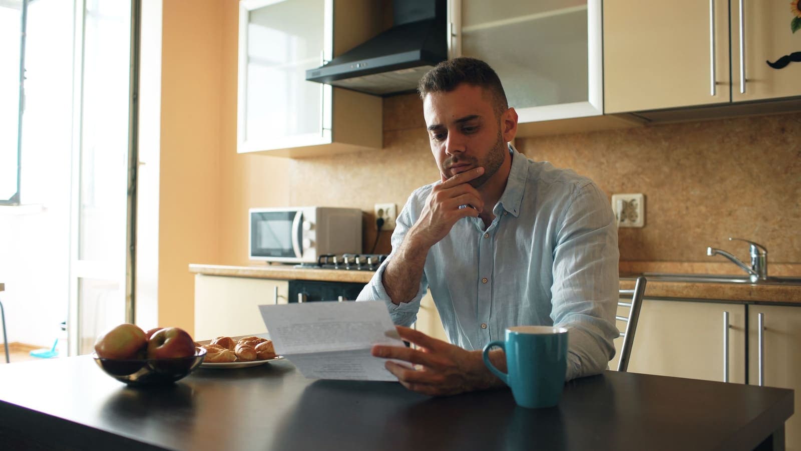 A man reads a letter at his kitchen table in morning light